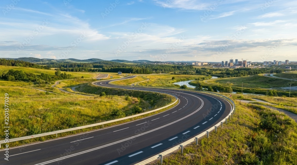 Fototapeta premium A winding highway curves through a lush green landscape towards a distant city skyline. The road is asphalt and bordered by a white safety barrier.
