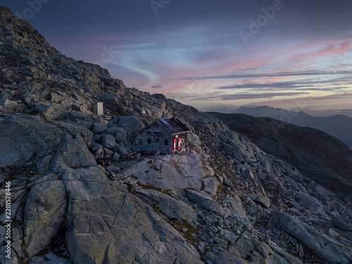 Mountain cabin on rocky terrain at dusk with colorful sky and distant mountains, Austria