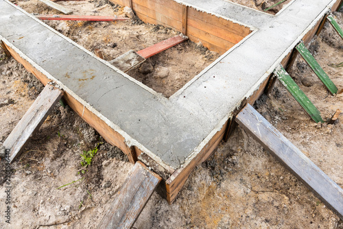 Concrete foundation footings poured into wooden formwork at a residential construction site, showing bracing, soil, and early-stage building layout for a new house foundation and structural base