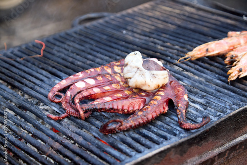 Fresh octopus and prawns cooking on a hot charcoal grill at a traditional Sicilian fish market of La Pescheria in Catania.