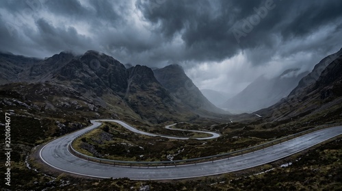 Winding mountain road through dramatic dark valley under stormy skies