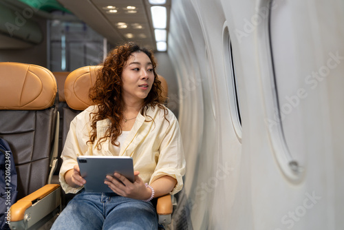 Foto Young Asian woman sitting near window inside passenger airplane holding digital