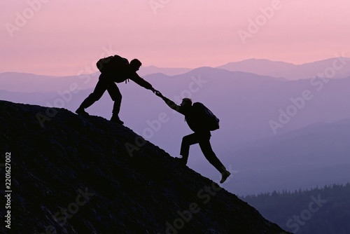 Silhouetted hikers helping each other climb a steep mountain ridge at sunrise