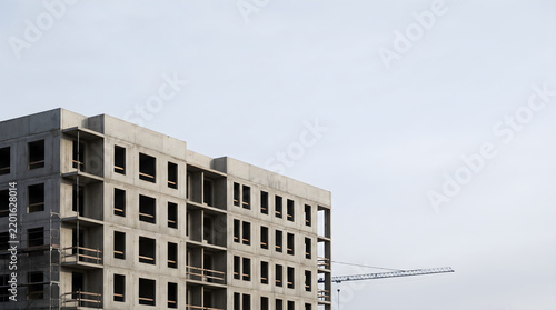Un immeuble chantier en construction avec du béton brut et des grues sur fond de ciel clair et lumineux.