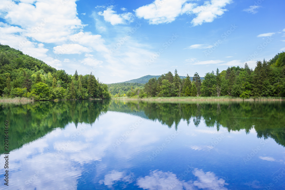 Obraz premium Blue lake mirrors a bright sky inside Plitvice Lakes National Park, Croatia