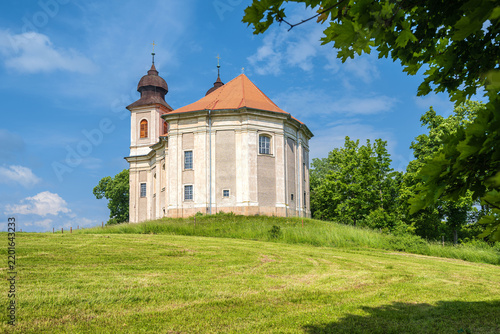 Grand Baroque Church of Saint Margaret standing isolated on a grassy hill under a blue sky in Sonov, Broumov region, Czech Republic.