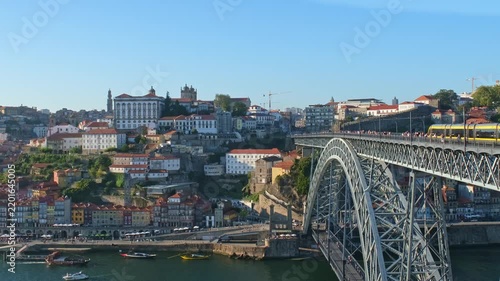 Video of a yellow tram crossing the upper deck of Dom Luis I bridge over the Douro river with Ribeira buildings in Porto, Portugal.