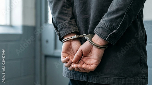 Man's hands cuffed behind back, crime arrest, justice concept, prison cell