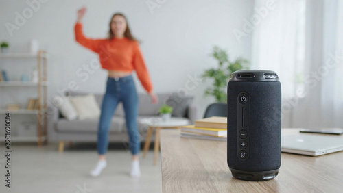 Young woman in casual clothing dancing in living room with portable speaker and natural light