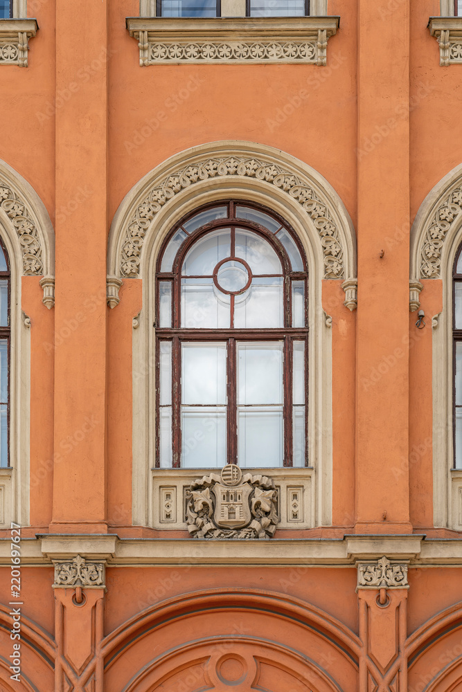 Obraz premium Ornate arched window with a carved coat of arms on a terracotta-colored historicist building facade in Budapest, Hungary