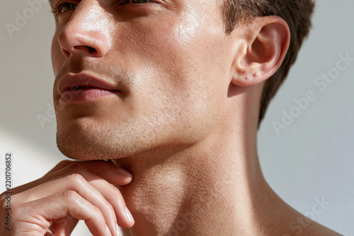 Young man touching neck in soft daylight with dewy skin and contemplative expression