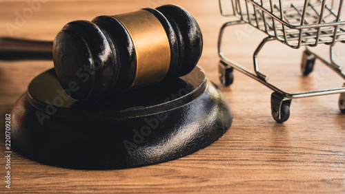 Wooden Judge Gavel and Sound Block Beside Miniature Shopping Cart on Wooden Surface Concept for Consumer Rights, Retail Regulations, and Commercial Law
