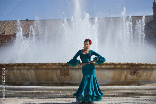 Young, brunette, Andalusian woman, beautiful, wearing a green flamenco dress and flowers in her hair, dancing flamenco, with a beautiful fountain behind her, in Spain Square in Seville.