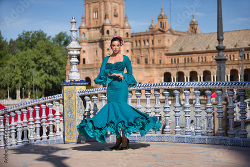 Young, brunette, Andalusian woman, beautiful, wearing a green flamenco dress and flowers in her hair, dancing flamenco on a pretty bridge in Spain Square in Seville.