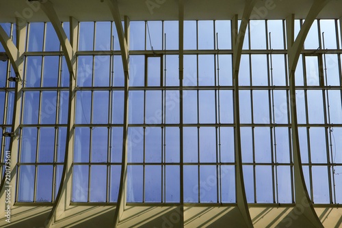 Large-scale glass paneling intersected by angular structural beams against a clear blue sky