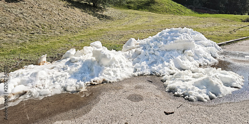 Foto Snow and ice pile melting on asphalt next to a green grassy hill, symbolizing th