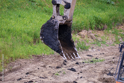 Heavy-duty excavator bucket hovers above loose soil amid green grass and excavated earth
