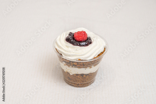 Obraz na płótnie Layered carrot cake cup with cream cheese frosting, berry compote, and a raspberry topper on a soft linen backdrop