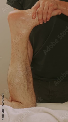 therapist cradles heel and supports calf during seated foot exam, with white towel under limb in clinical room