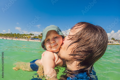 Dad plays with his infant in warm turquoise sea, capturing fatherhood, baby swimming, family travel and tropical beach holiday concept