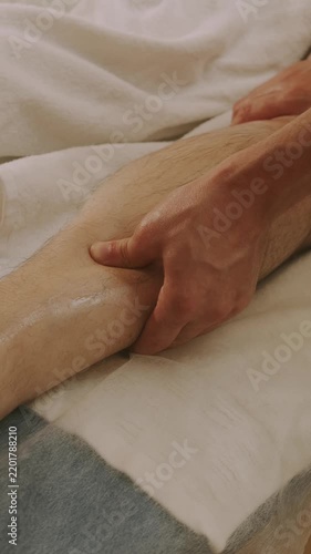 close-up hands massage calf with oil sheen, thumbs pressing during manual therapy warm light on skin and towel