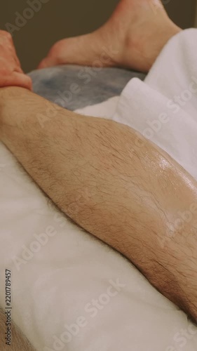 closeup view of therapist hands applying firm thumb pressure and gliding strokes on oily hairy calf warm light