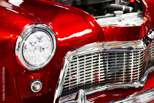 Red vintage automobile front with round headlight, chrome grille, glossy curved bodywork, exposed engine compartment, and classic automotive design detail