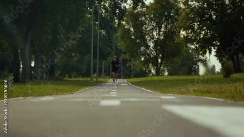 Runner jogging along treelined park path under warm daylight in low angle outdoor fitness scene view