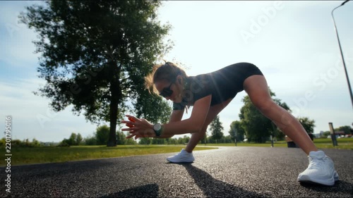 Athletic woman holding forward fold stretch on park path with bright backlit morning sky above trees