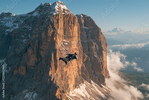 Person in a wingsuit flying near mountain cliffs during sunset in the Dolomites