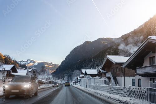 Scenic alpine village resort in Austria gondola cablecar above snowy road car parking lots trees mountain valley scenery under clear blue winter sky. Scene winter tourism destination