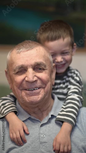 Great-grandson hugs great-grandfather from behind, they smile together with love and warmth.