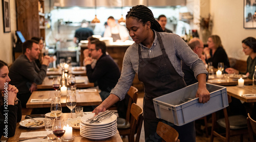 Server clearing empty plates from a table in a busy restaurant  