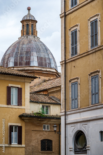 Traditional roman residential buildings with window shutters and the historic dome of the Santa Maria in Aquiro church in the background in Rome, Italy.