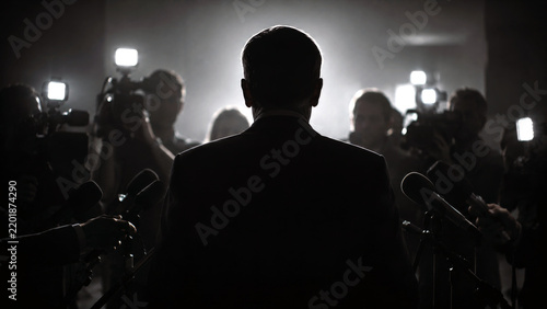 Silhouette of a businessman facing reporters and microphones at a press conference, representing media attention, public relations, leadership, and corporate news