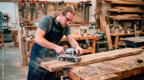 Carpenter working with sander on wooden plank in workshop, skilled craftsman using electric sander for smooth finish on lumber, creating high-quality wood products for interior design.