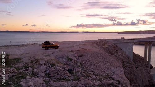Cinematic aerial drone view of Pag Bridge in Croatia at sunset, featuring the dramatic rocky landscape of Pag Island, Adriatic Sea, rugged coastline, and warm golden evening light