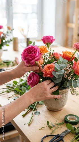 Close-up view of hands learning to arrange vibrant garden roses and eucalyptus during an interactive and inspiring floral design master class, artistic, foliage, learning process
