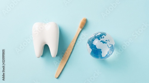 Minimal dental care concept with a white tooth shape, toothbrush, and globe on a pastel blue background, symbolizing global oral health, hygiene, prevention, and dentistry.
