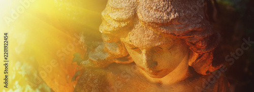 Ancient stone angel statue illuminated by radiant golden sunlight, symbolic image of heaven, divine light, faith, hope and eternal peace.