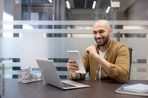 Businessman using tablet and laptop for financial analysis in modern office, professional man working at desk with digital devices for corporate communication