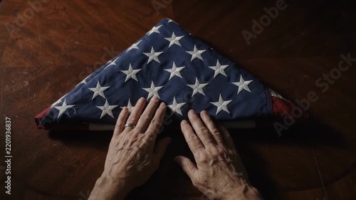Tribute to female veteran with folded American flag on wooden table, honoring sacrifice during Memorial Day. Hands gently place flag, symbolizing respect and remembrance for female veterans.