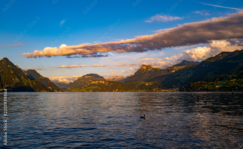 Fototapeta premium Swiss mountain lake beneath cumulus clouds. Swiss Alps cloudscape over Lake Lucerne. Summer tourism with Swiss alpine mountain views. Moody landscape with Swiss lakeside nature.