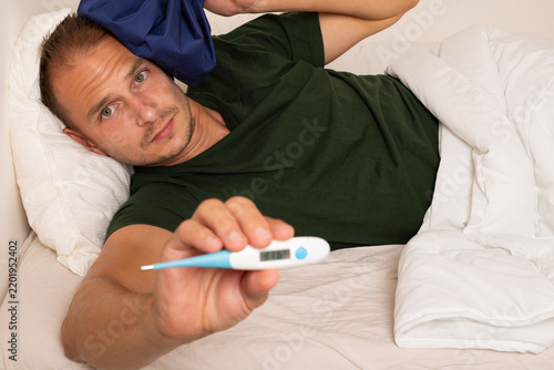 Sick Man Checking His Temperature with Digital Thermometer in Bed