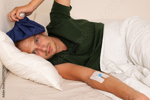 Sick Man with IV Cannula and Cold Compress Resting in Bed