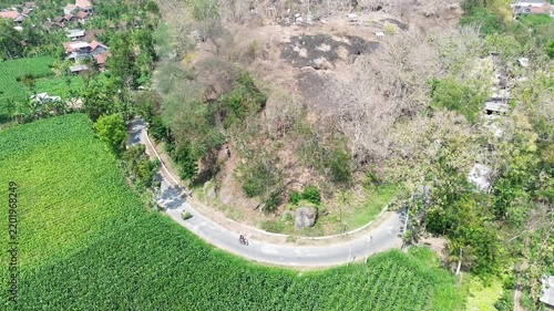 Aerial drone view of winding curved asphalt road along green corn field and rocky hill in rural countryside. Motorbike riding on country road video footage template for travel banner.