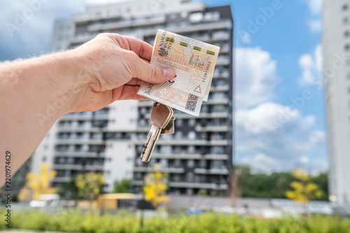 Close up of Hand Holding Keys and Polish Zloty Money Bills in Front of Residential Complex