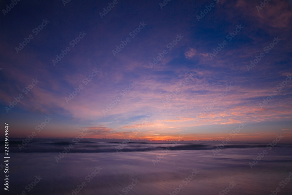 Obraz premium Tranquil ocean sunset with silky water ripples under a dramatic purple and pink twilight sky scenic beach landscape 