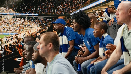Cuadro en lienzo Tense blue team supporters react to a close call during a live soccer match in a crowded stadium while waiting for the final whistle, showing suspense and anticipation across the group