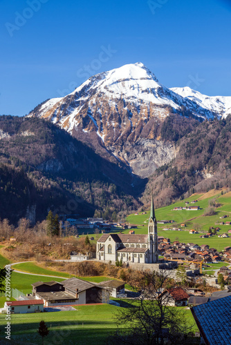 Lungern village surrounded by the Swiss Alps, with snow-covered mountain peaks rising behind the settlement. The scenic landscape is located in Obwalden canton, Switzerland.